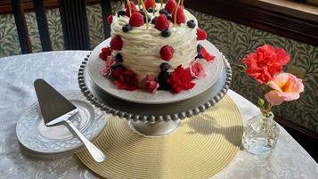 A cake with fruit on a stand, a cake server, and a vase with flowers on a table.