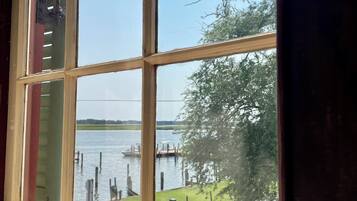 A window with a view of a body of water, dock, and grassy area.