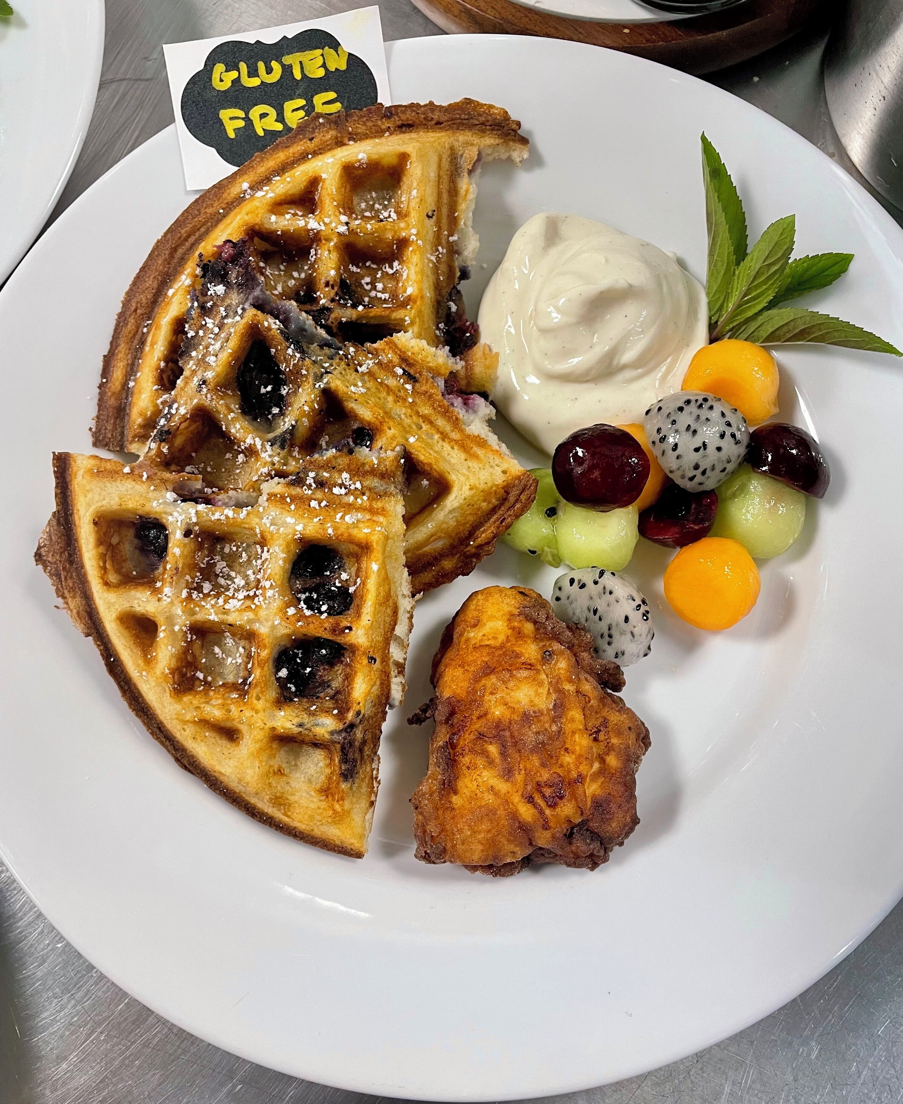 A plate with waffles, fruit, and a chicken piece.