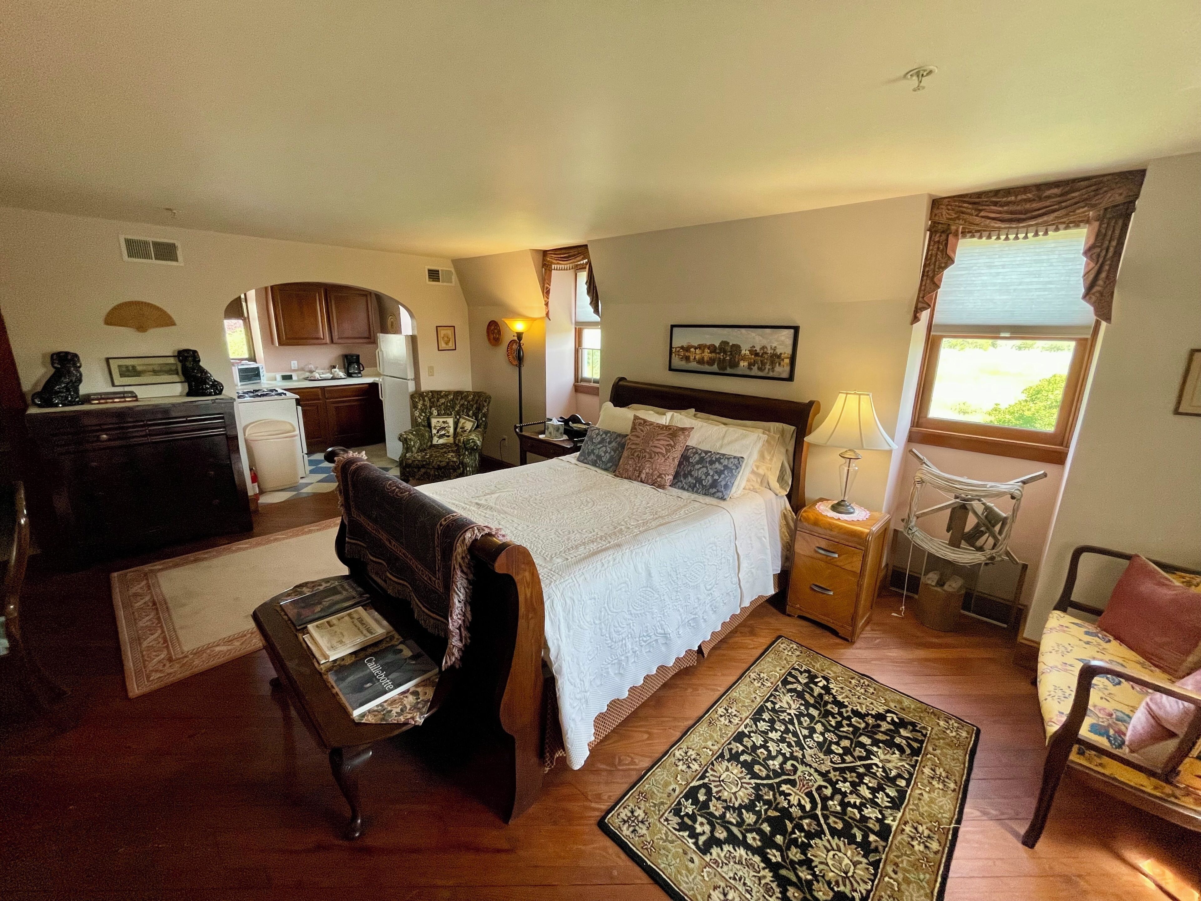 Une chambre à coucher comprenant un lit, des tables de chevet, une chaise, un bureau, une lampe, une fenêtre et une vue sur l’extérieur.