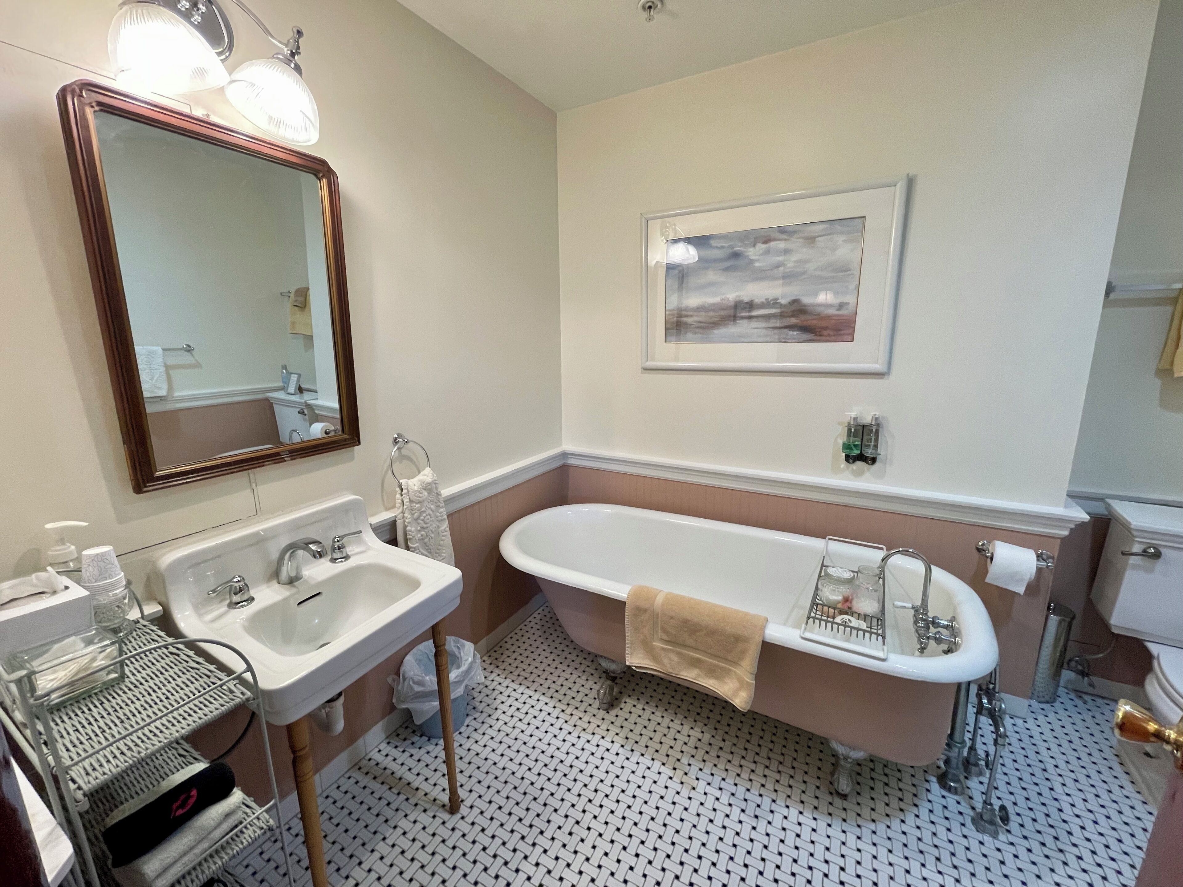 A bathroom with a sink, mirror, bathtub, and a framed picture on the wall.
