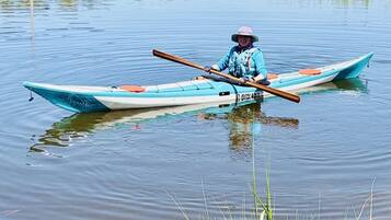 A person in a canoe on a calm body of water with grassy banks and trees in the background.
