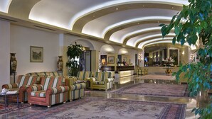 Eine geräumige Lobby mit einer Rezeption, mehreren Sitzbereichen und einer großen Zimmerpflanze.