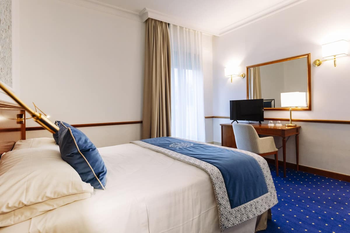 A hotel room with a bed, a desk, a chair, a television, and a mirror.