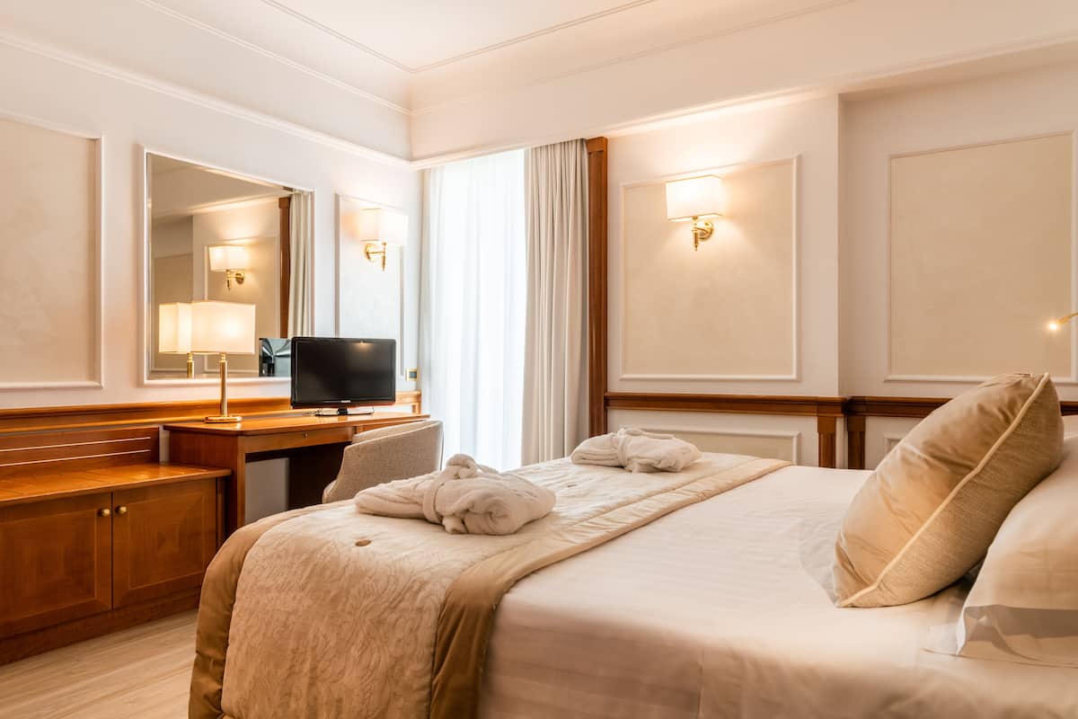 A hotel room with a bed, a desk, a television, and a mirror.