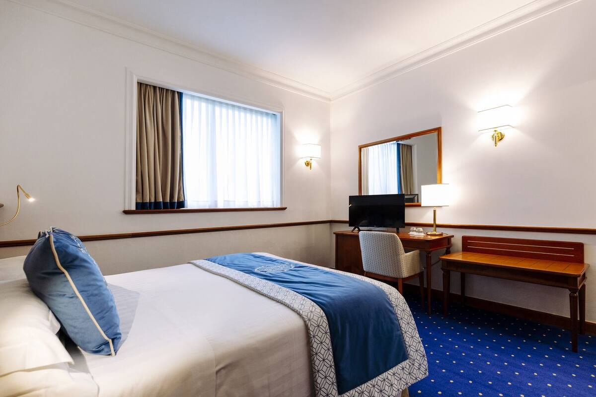 A hotel room with a bed, a desk, a chair, a television, and a mirror.