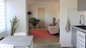 Un espacio habitable compacto con kitchenette, comedor y zona de estar con alfombra roja.