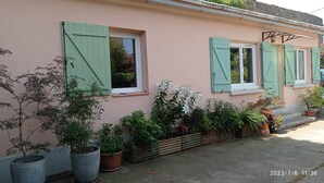 Un edificio rosa con contraventanas verdes, plantas en macetas y un sello de fecha de 2023/7/6 11:36.