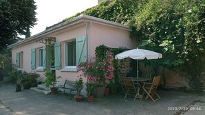 Una casa con un patio, una mesa con sillas y una sombrilla blanca.
