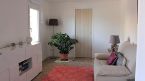 Una sala de estar moderna con un sofá, una alfombra roja, una planta en maceta, una lámpara y un aparador blanco.
