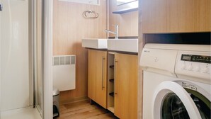 Cocina compacta con lavadora integrada, armarios de madera y ventana sobre el fregadero.