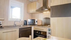 Una cocina compacta con armarios de madera, campana extractora de acero inoxidable, microondas y horno empotrado.