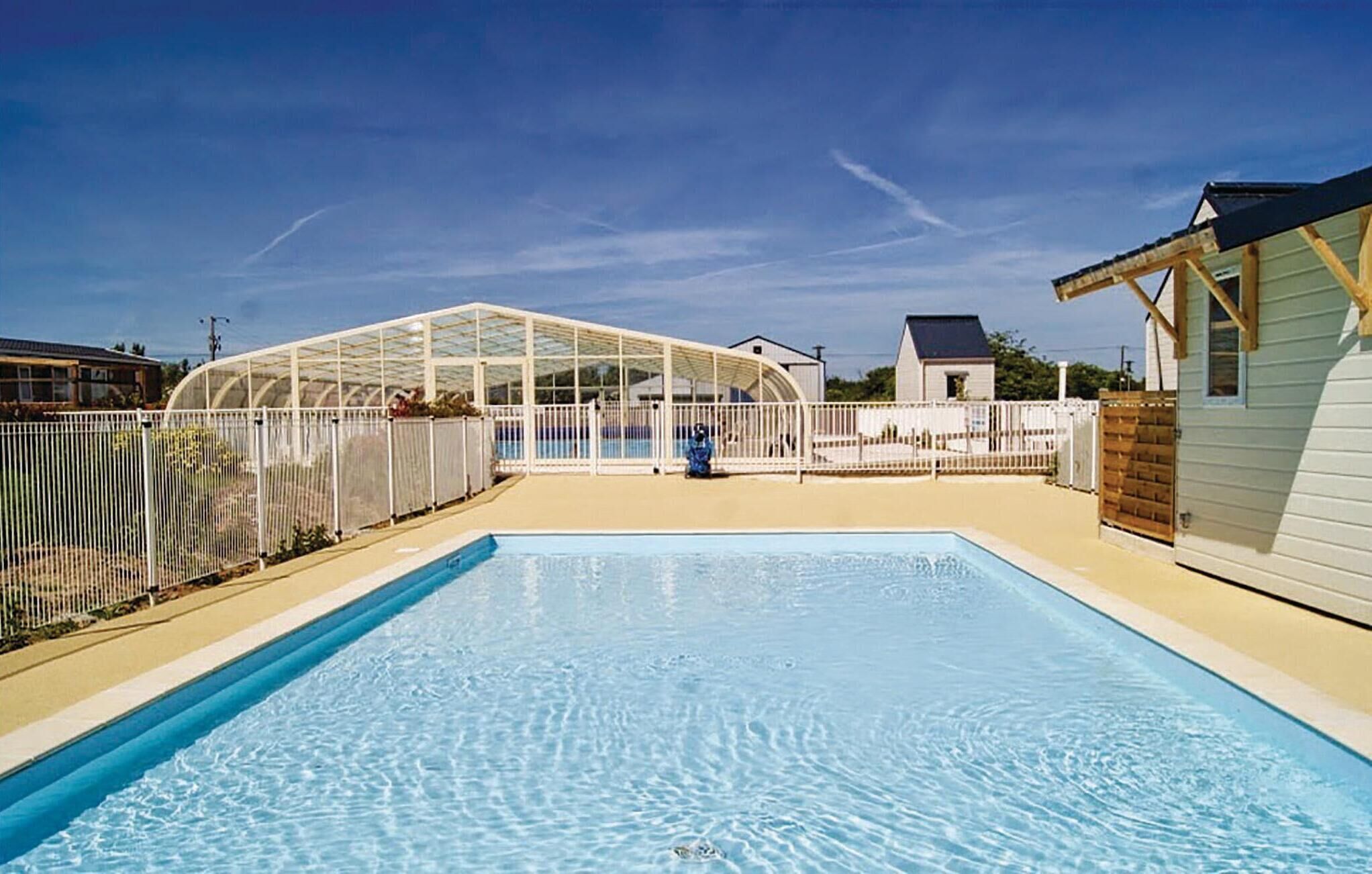 A swimming pool with a glass enclosure, surrounded by a white fence, and a small house in the background.