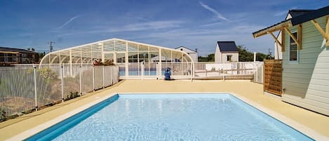 A swimming pool with a glass enclosure, surrounded by a white fence, and a small house in the background.