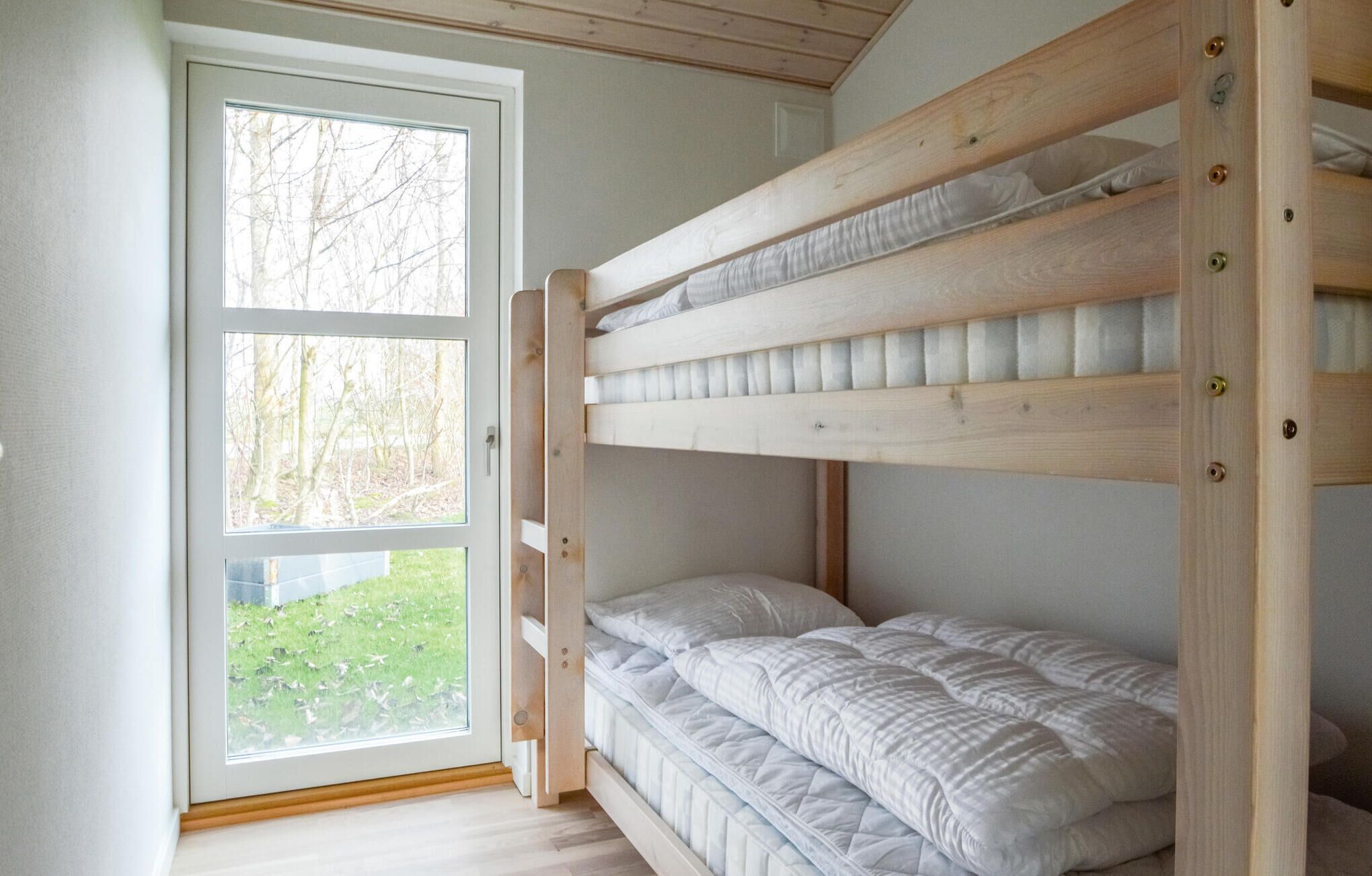 A bunk bed with a view of a grassy area through a window.