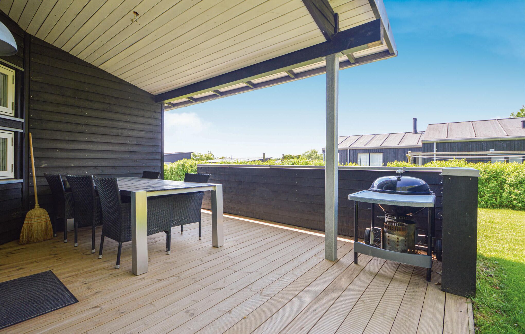 Une terrasse extérieure couverte, équipée d’une table et de chaises, d’un barbecue et offrant une vue sur les environs.