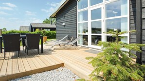 A modern outdoor deck with a wooden floor, two wicker chairs, a lounge chair, and a small potted plant. - 3 bedroom amazing home in Haderslev (Haderslev)