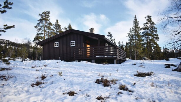Una cabaña de madera con un porche, rodeada de nieve y árboles.