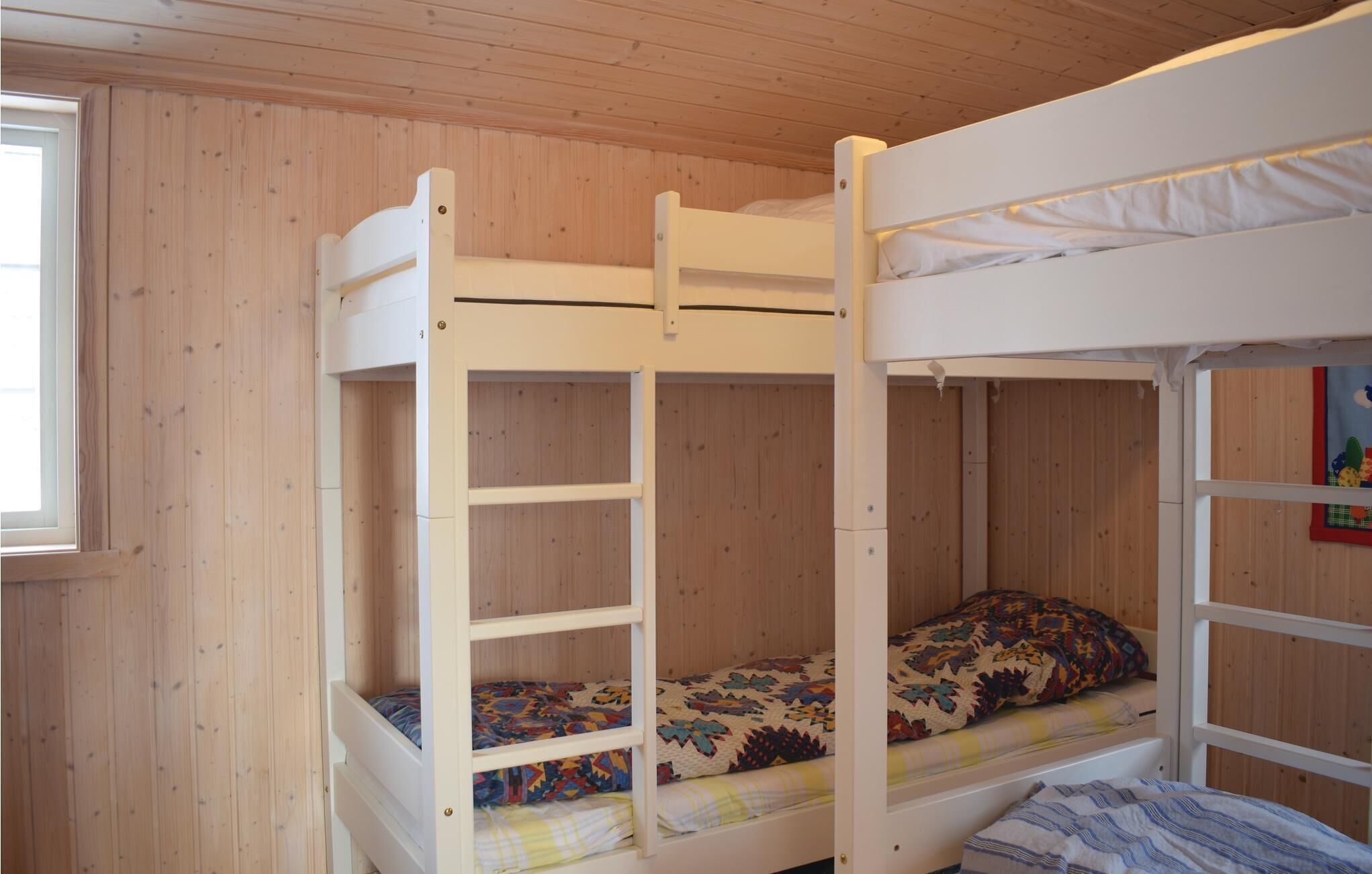 Una cama litera con escalera, ventana y pared de madera.