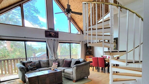 Un soggiorno spazioso con soffitto in legno, ampie finestre, un divano, un tavolino da caffè e una scala a chiocciola.