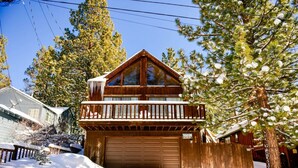 Una baita di legno a due piani con un balcone, un garage e un paesaggio innevato.