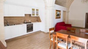 A compact kitchen with white cabinets, a red sofa, and a dining table.