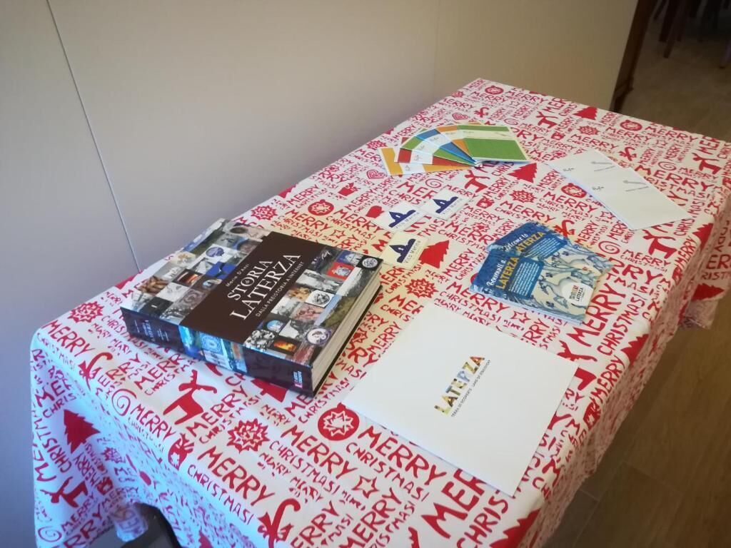 A table with a Christmas-themed tablecloth, a book titled 'Storia Latente', and a fan.