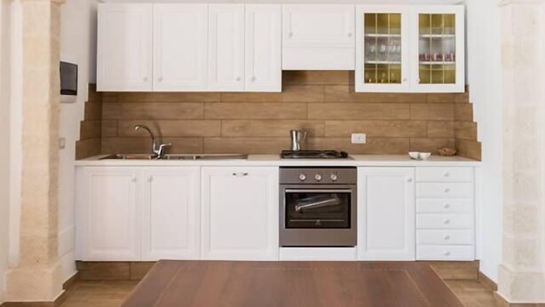 A kitchen with white cabinets, a wooden countertop, and an archway.