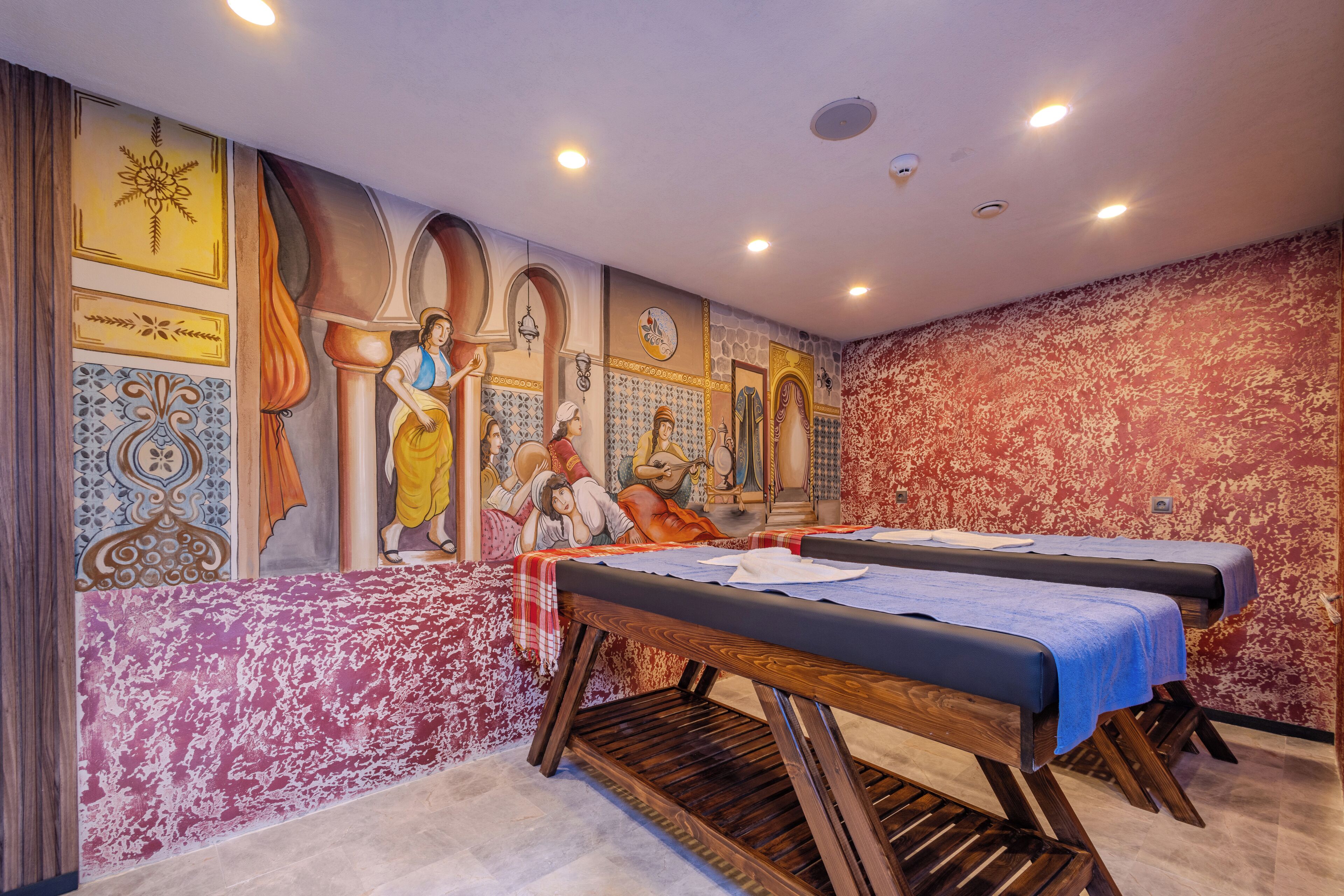 A room with two massage tables, a mural with religious figures, and a patterned wall.