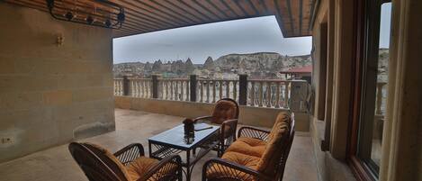 A balcony with wicker furniture and a table, overlooking a mountainous landscape.