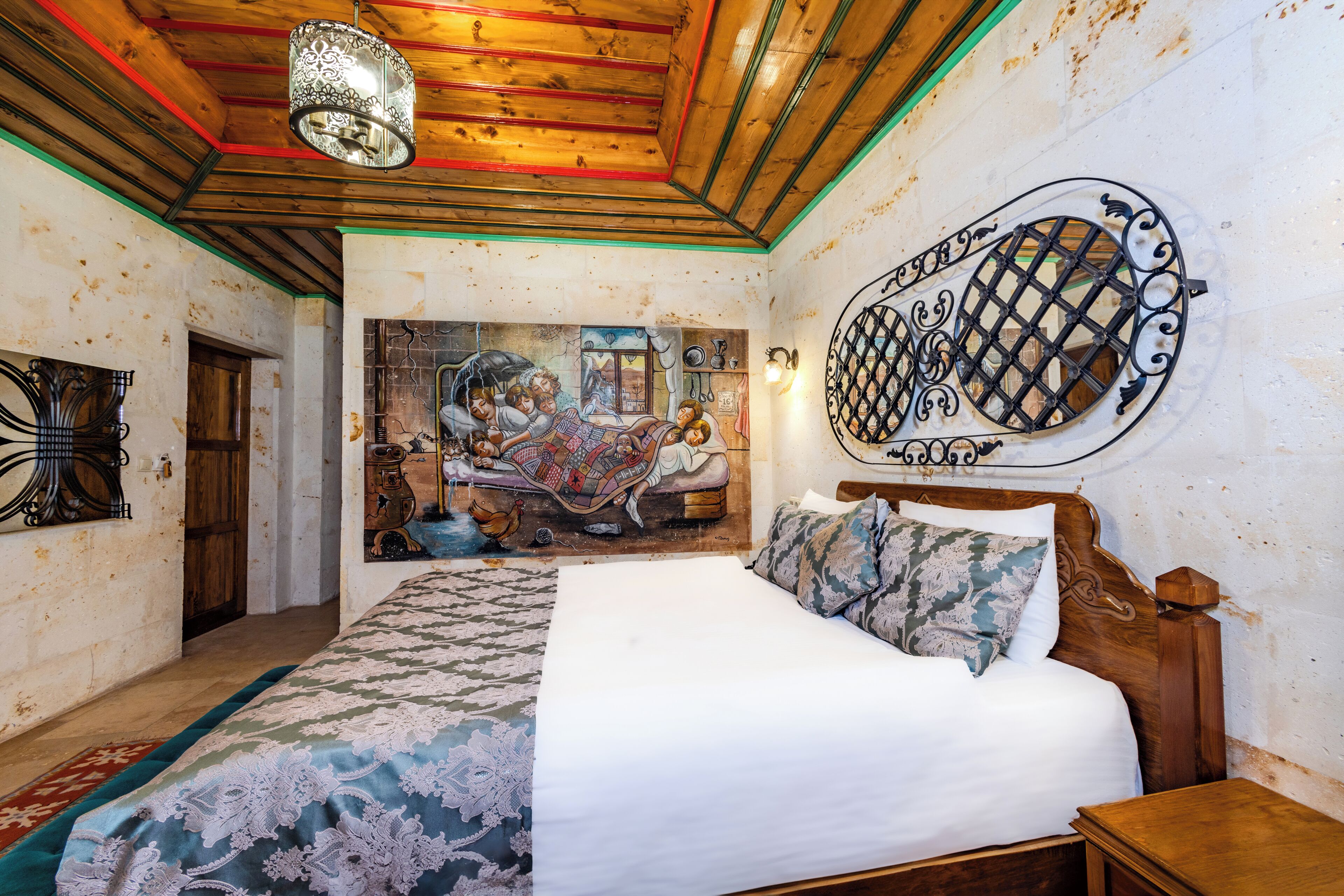 A bedroom with a large bed, a wooden headboard, a decorative wall piece, and a mural on the wall.