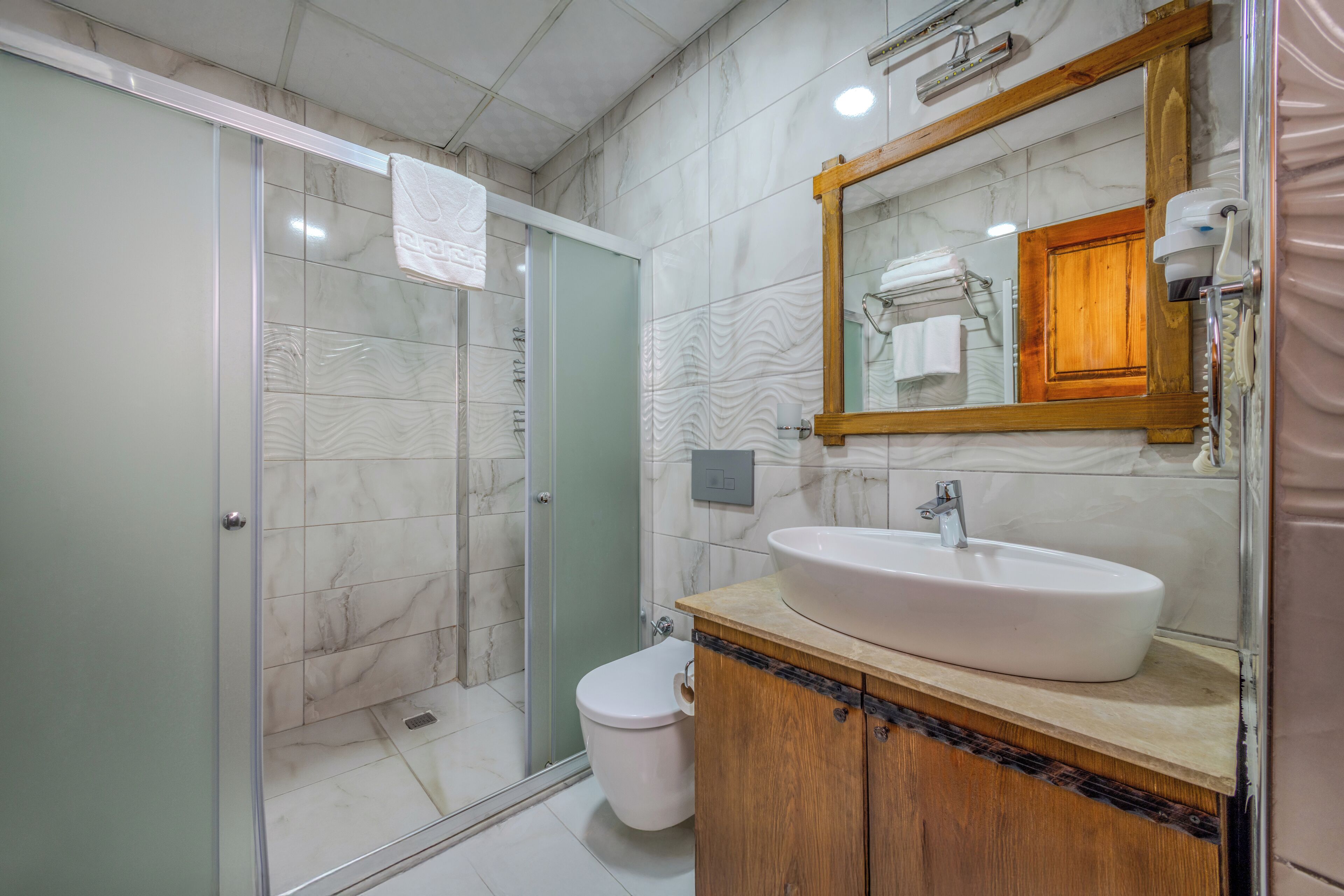 A bathroom with a glass shower enclosure, a white sink with a wooden cabinet, and a mirror with a wooden frame.