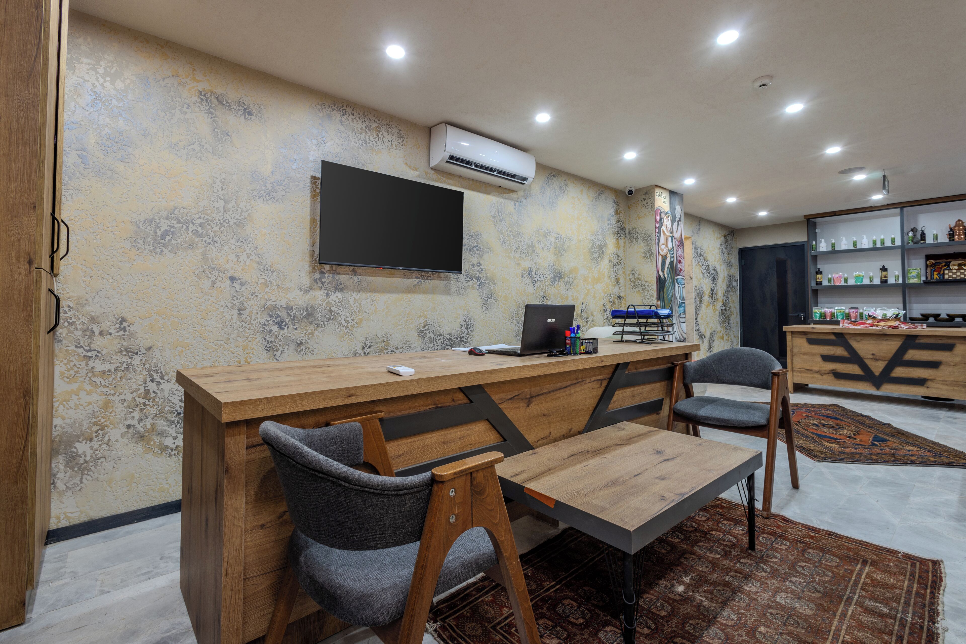 A modern office space with a wooden desk, two chairs, a computer, and a mounted TV.