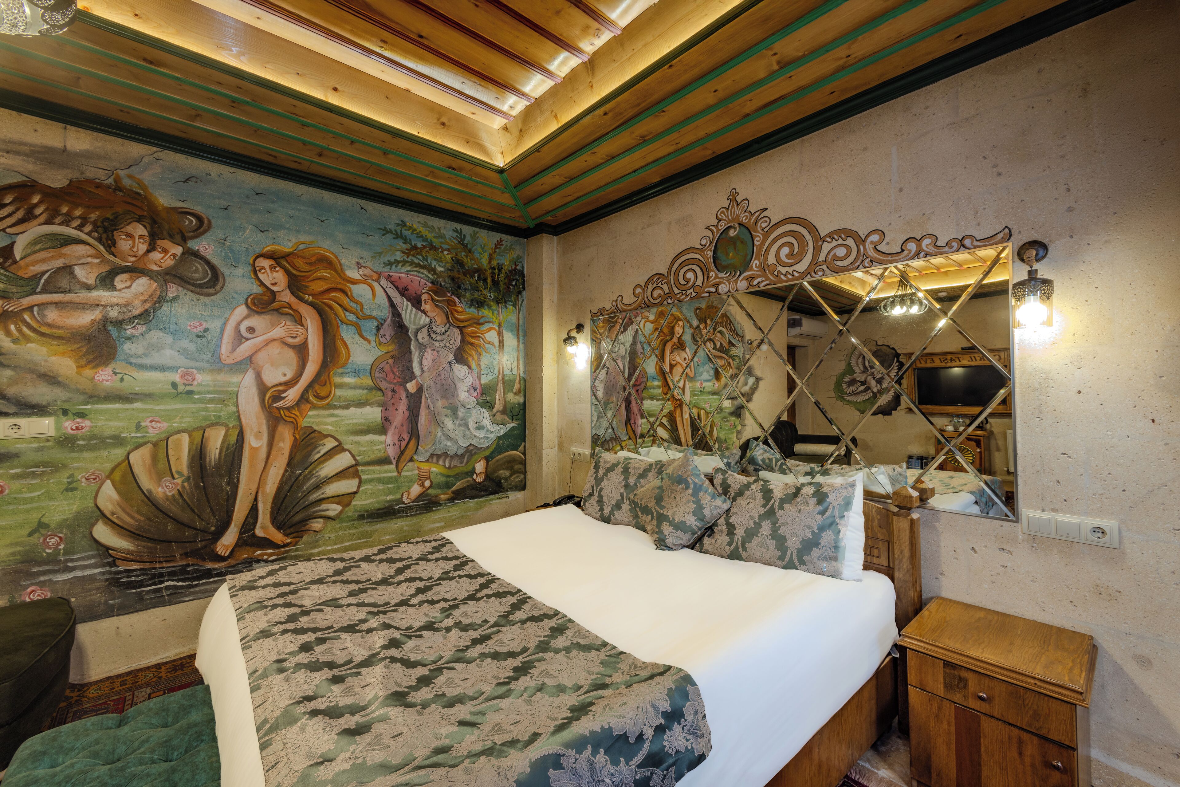 A bedroom with a mural, a bed with patterned bedding, a wooden nightstand, and a mirror with a decorative frame.