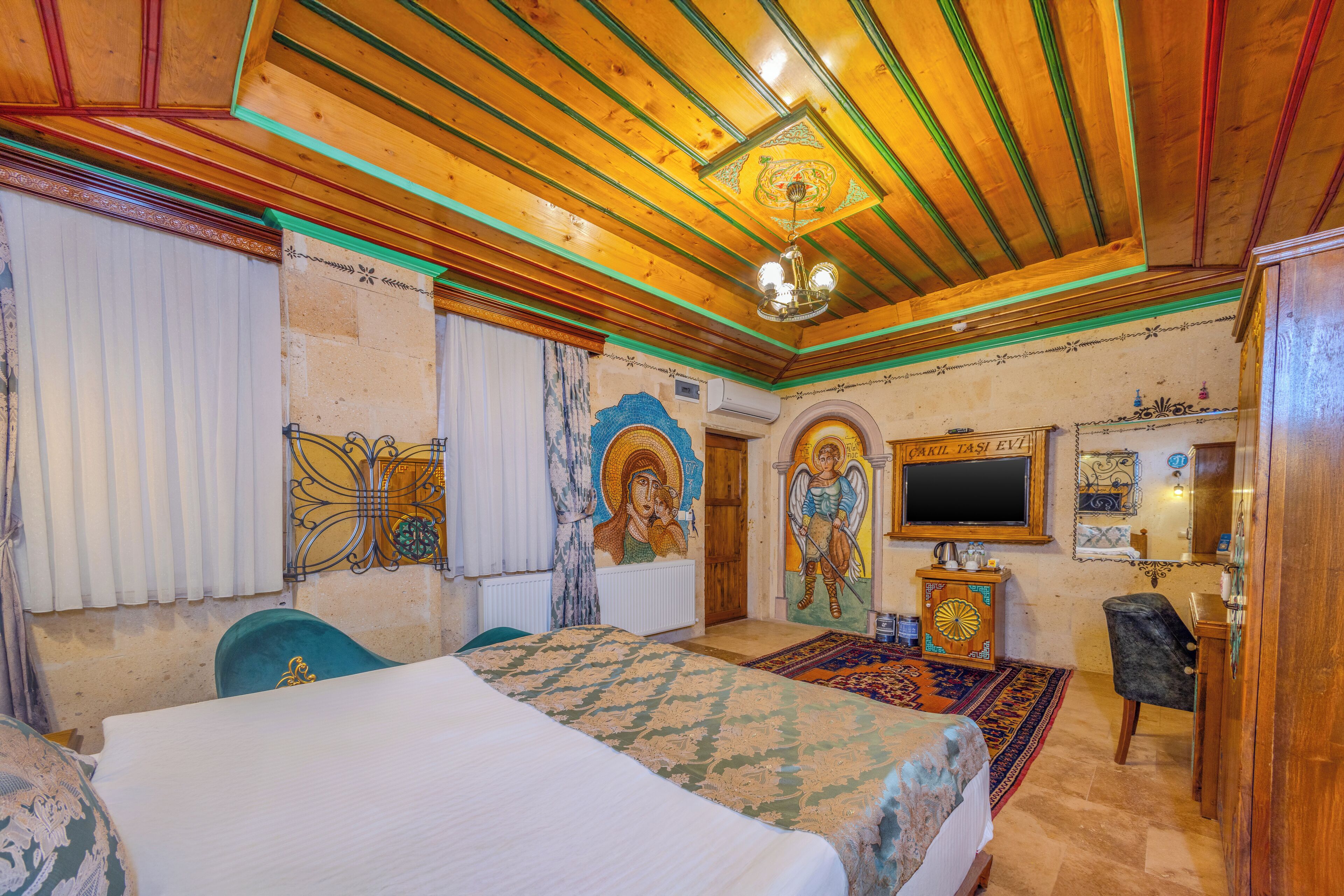 Quarto com teto de madeira, cama, escrivaninha e televisão.