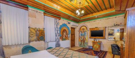 Quarto com teto de madeira, cama, escrivaninha e televisão.