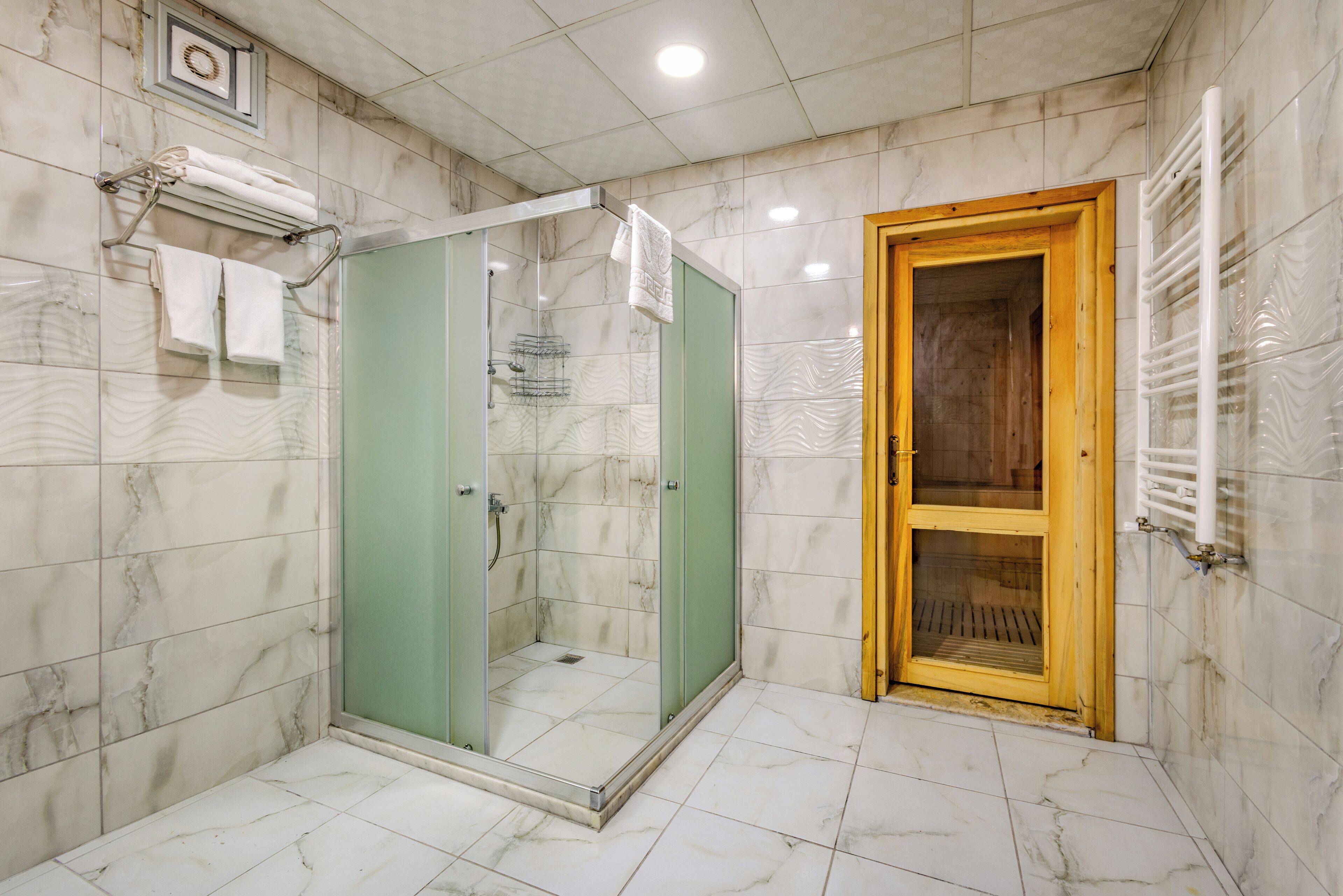 A bathroom with a glass-enclosed shower, a wooden door, and marble tiles.
