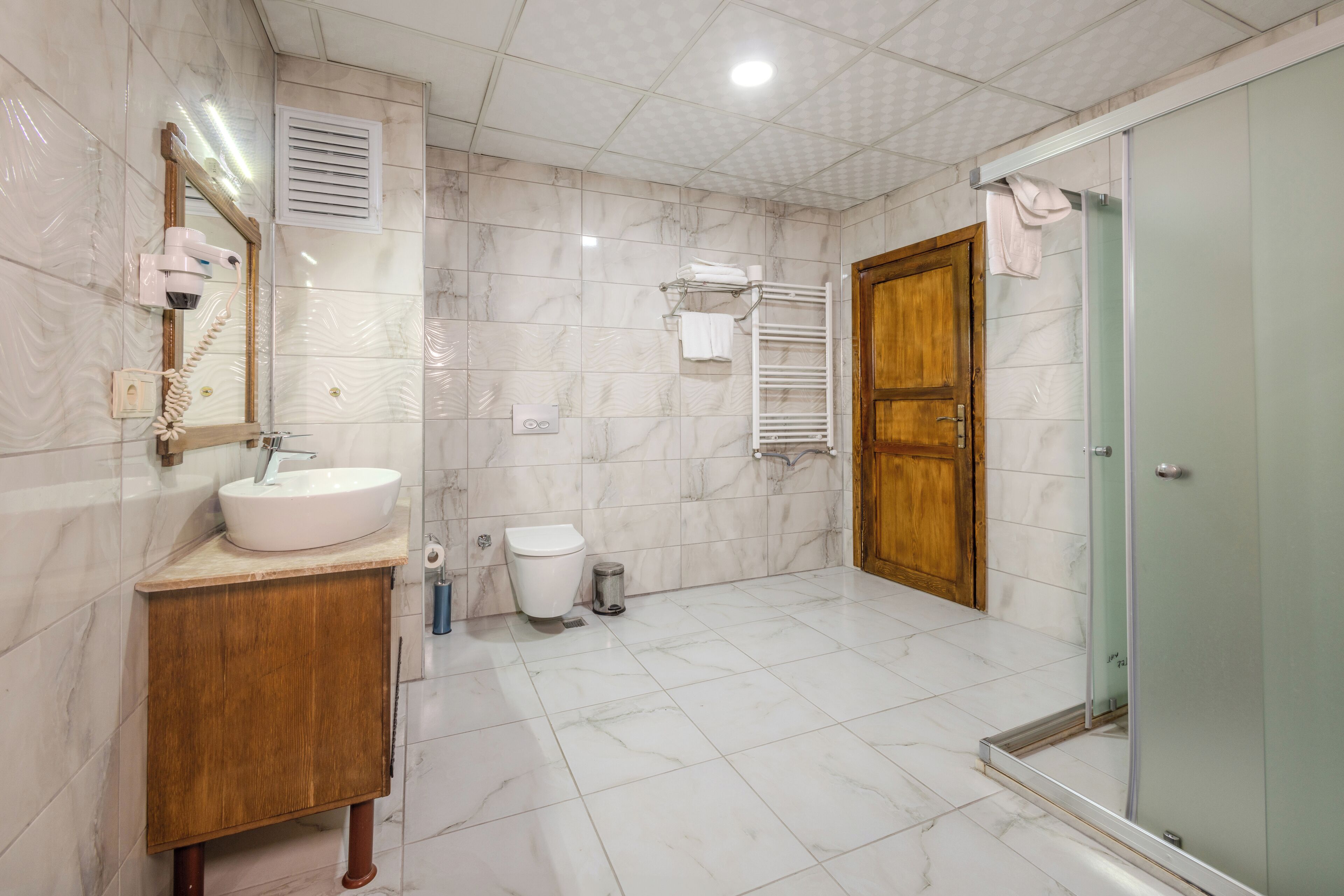 A modern bathroom with a marble floor, wooden vanity, white sink, and a glass shower enclosure.