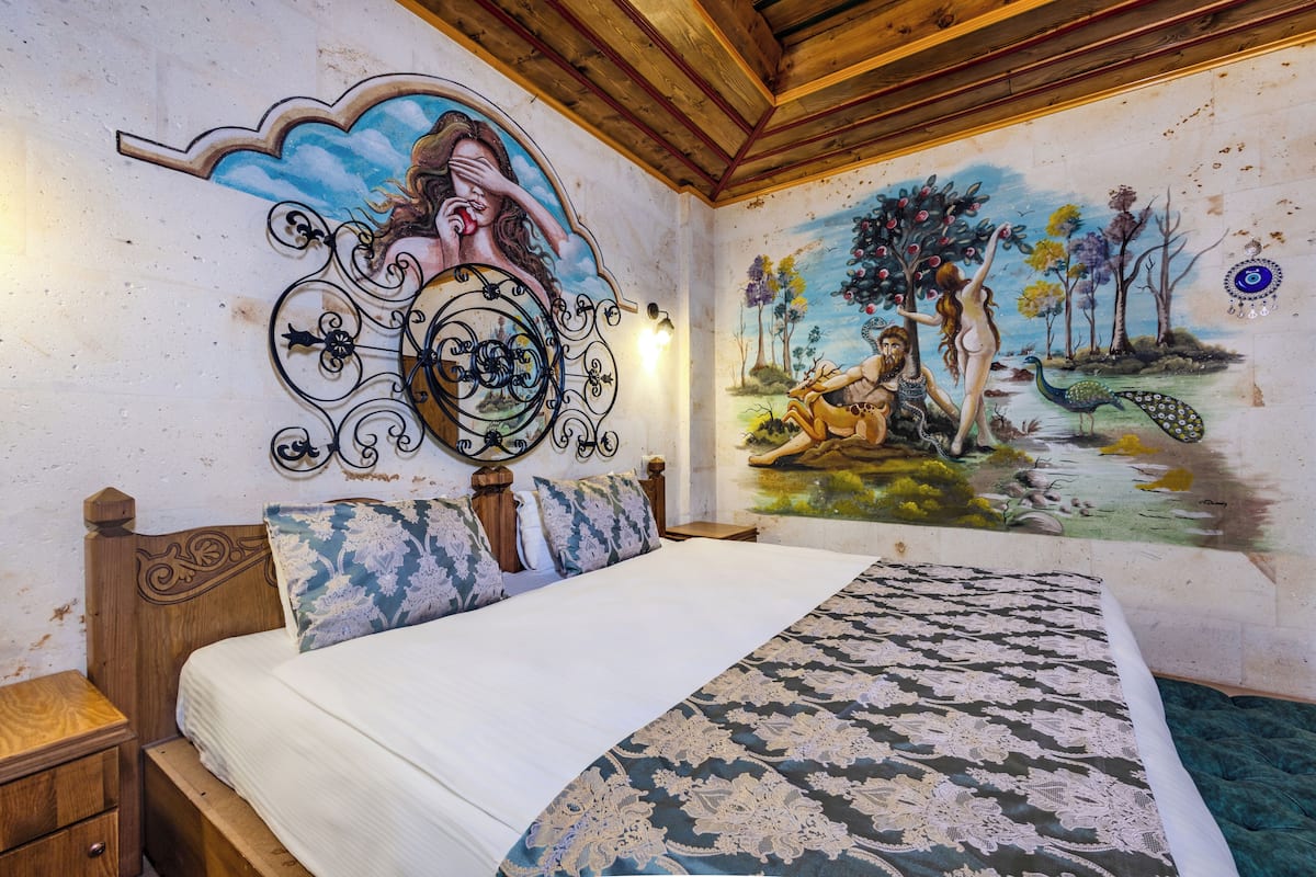 A bedroom with a large bed, a wooden headboard, a decorative wall mirror, and a mural depicting a nature scene.
