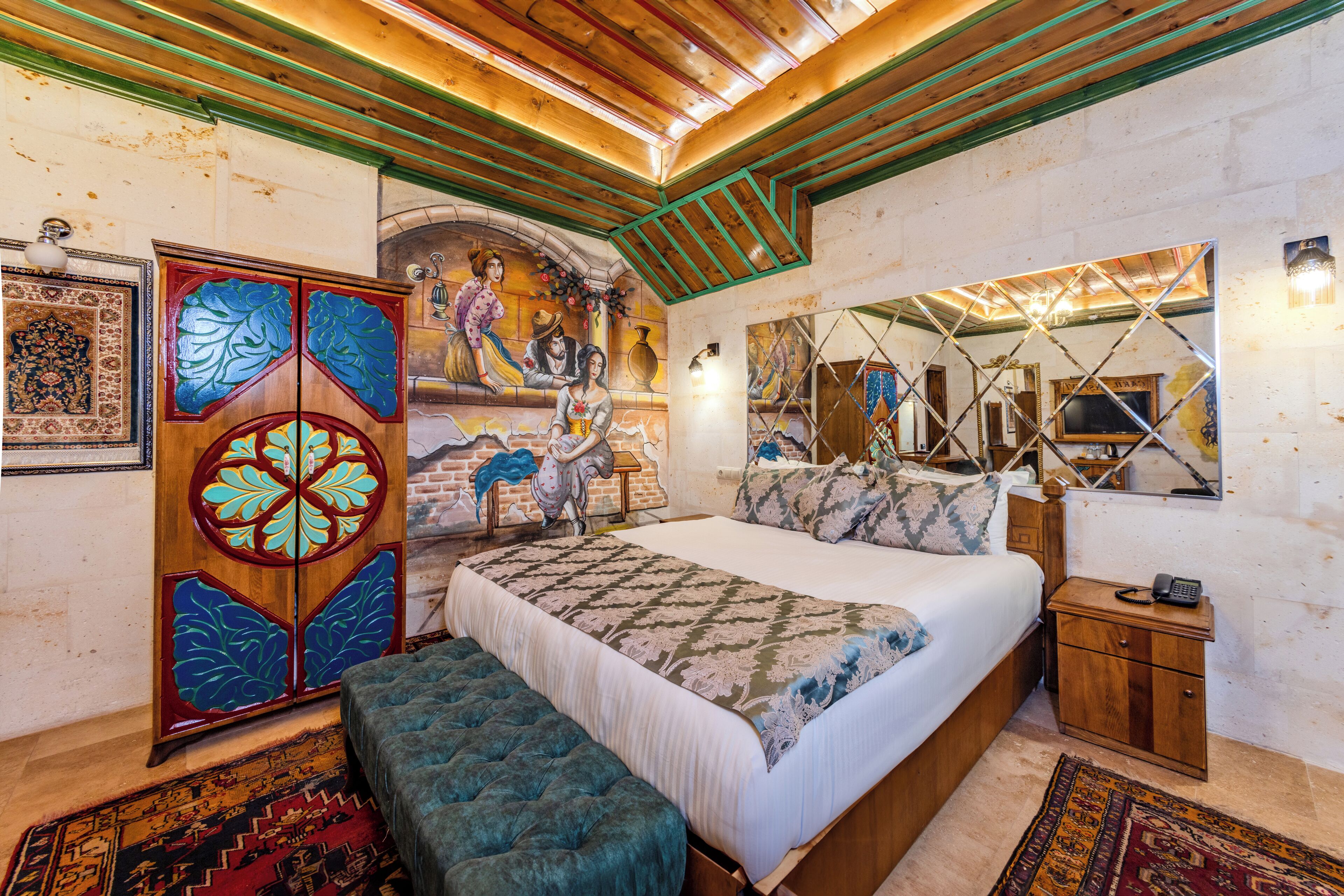 Un dormitorio con una cama grande, una mesita de noche de madera, un banco, un aparador decorativo y un mural en la pared.
