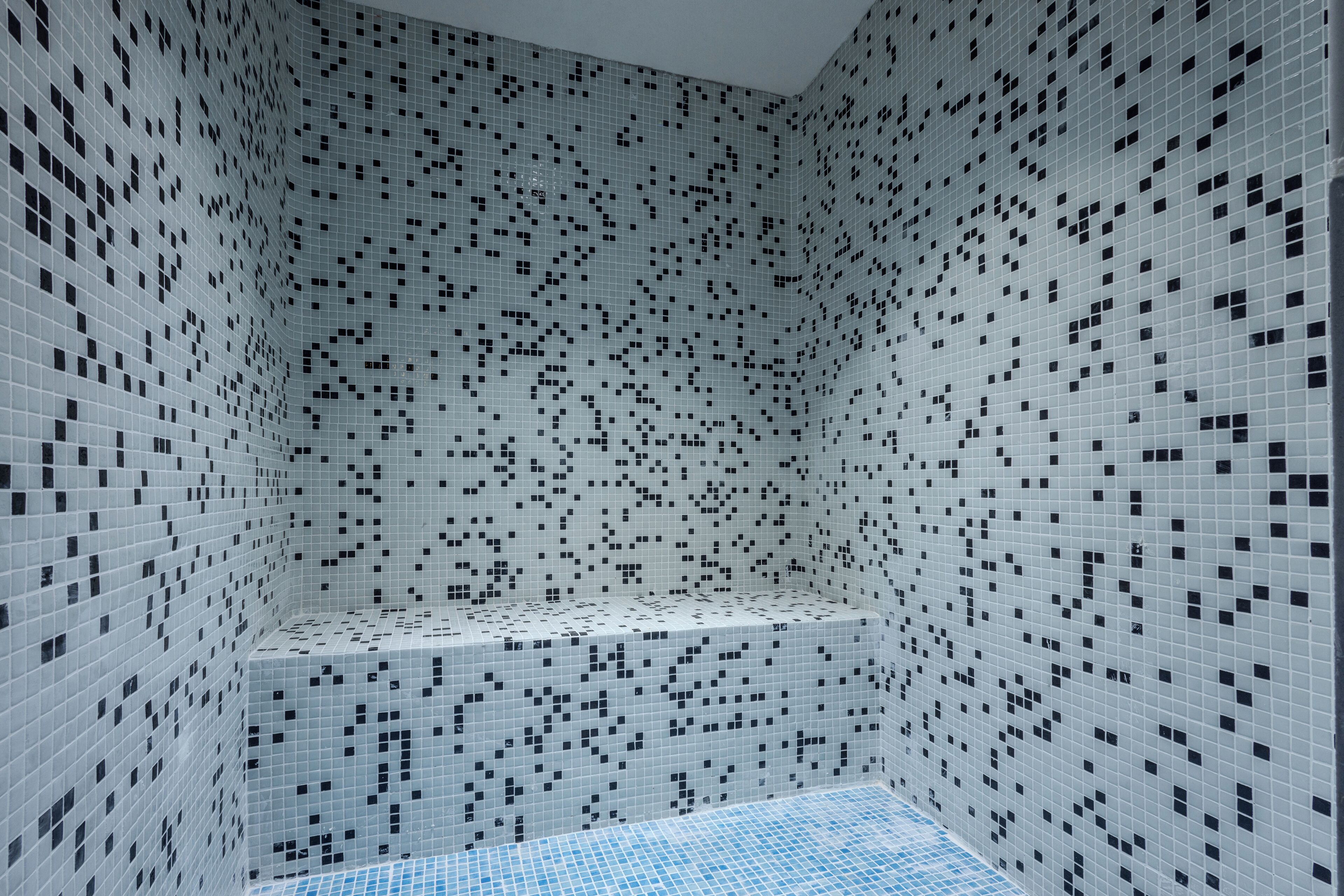 Un espacio de ducha con azulejos, suelo azul y un banco.