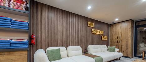 Un hall d’hôtel moderne avec un canapé modulable, des murs recouverts de panneaux en bois et un extincteur bien visible.