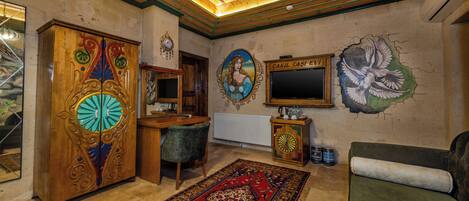 Una habitación con techo de madera, un espejo grande, un tapiz rojo estampado, un sofá verde y una pared con un mural de pájaros.
