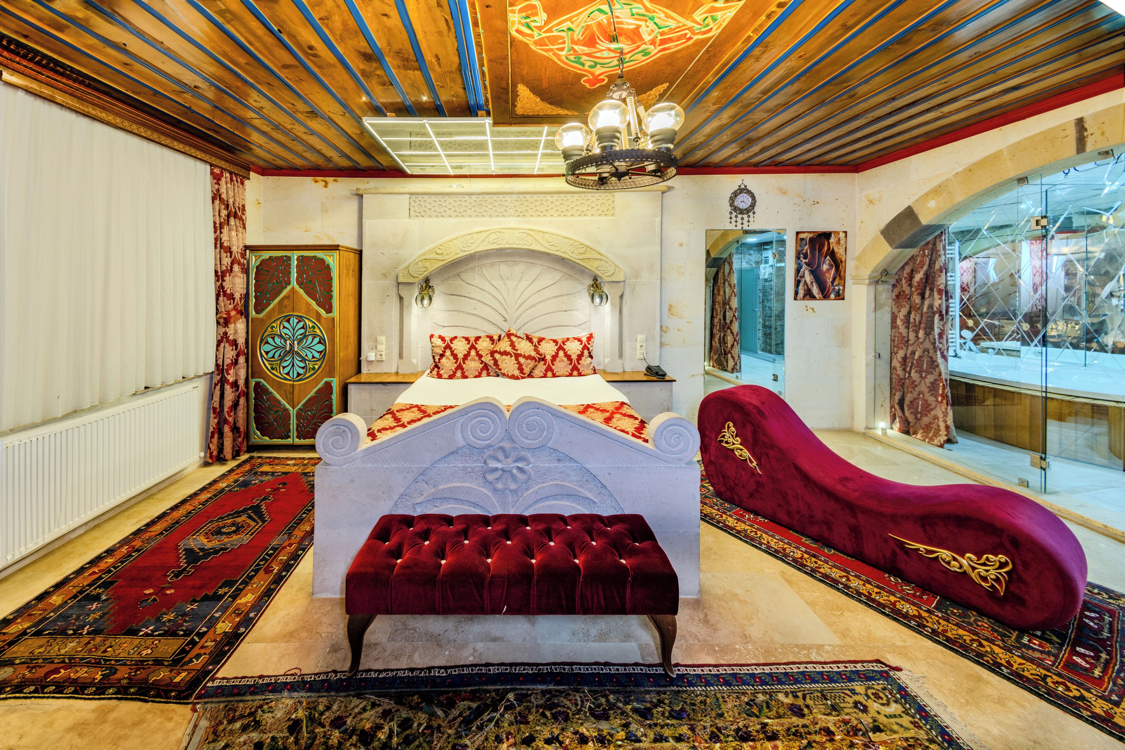 Un dormitorio con una cama grande, un sillón de terciopelo rojo y vistas de la ciudad a través de un ventanal.