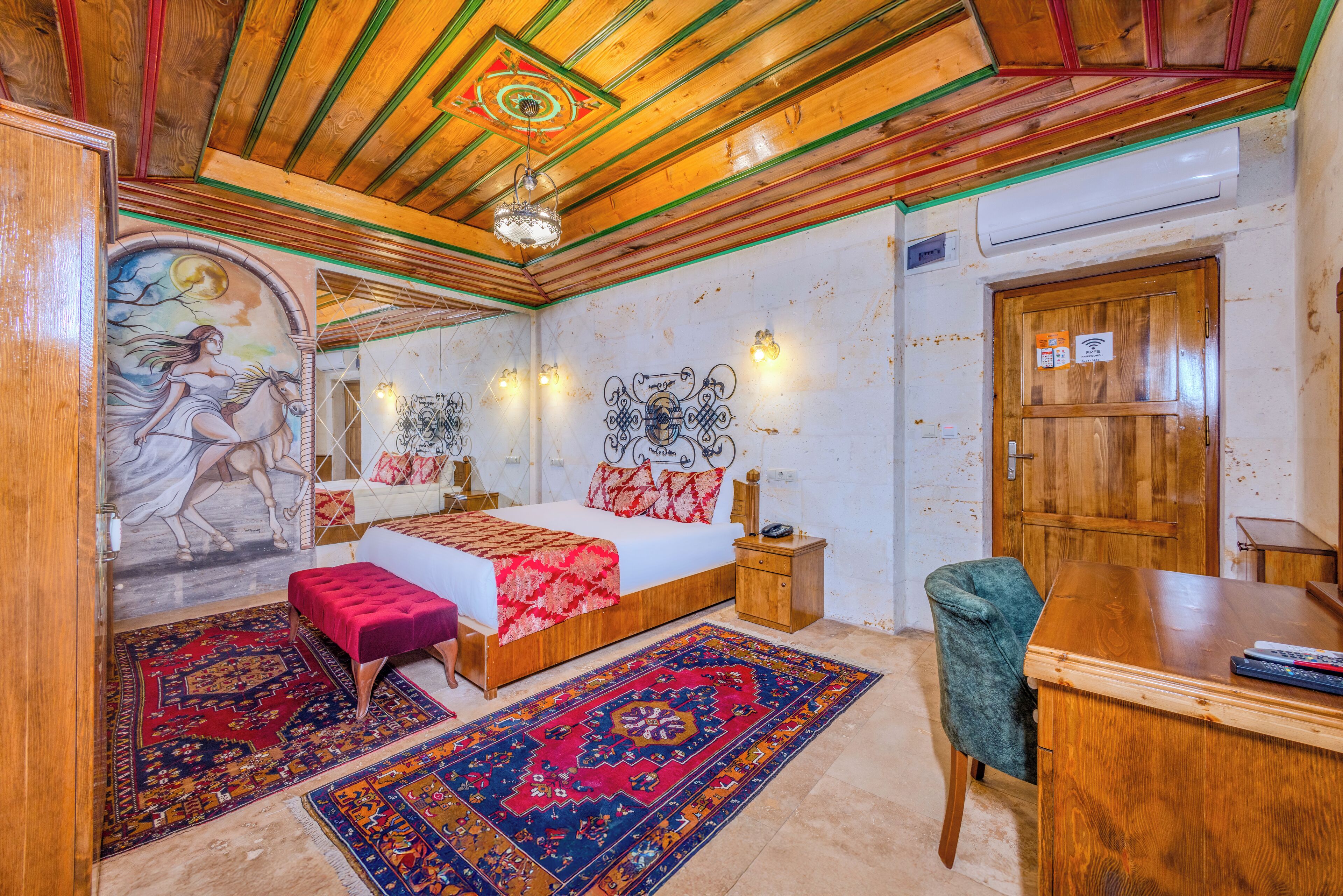 Une chambre avec un plafond en bois, un lit recouvert d’une couette rouge et blanche, un bureau et une chaise.