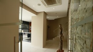 A modern hotel lobby with a stone wall, a wooden sculpture, and a staircase.