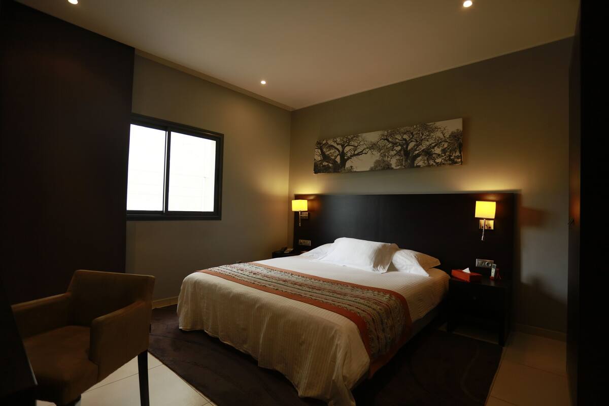 A hotel room with a large bed, two bedside lamps, a chair, and a window.