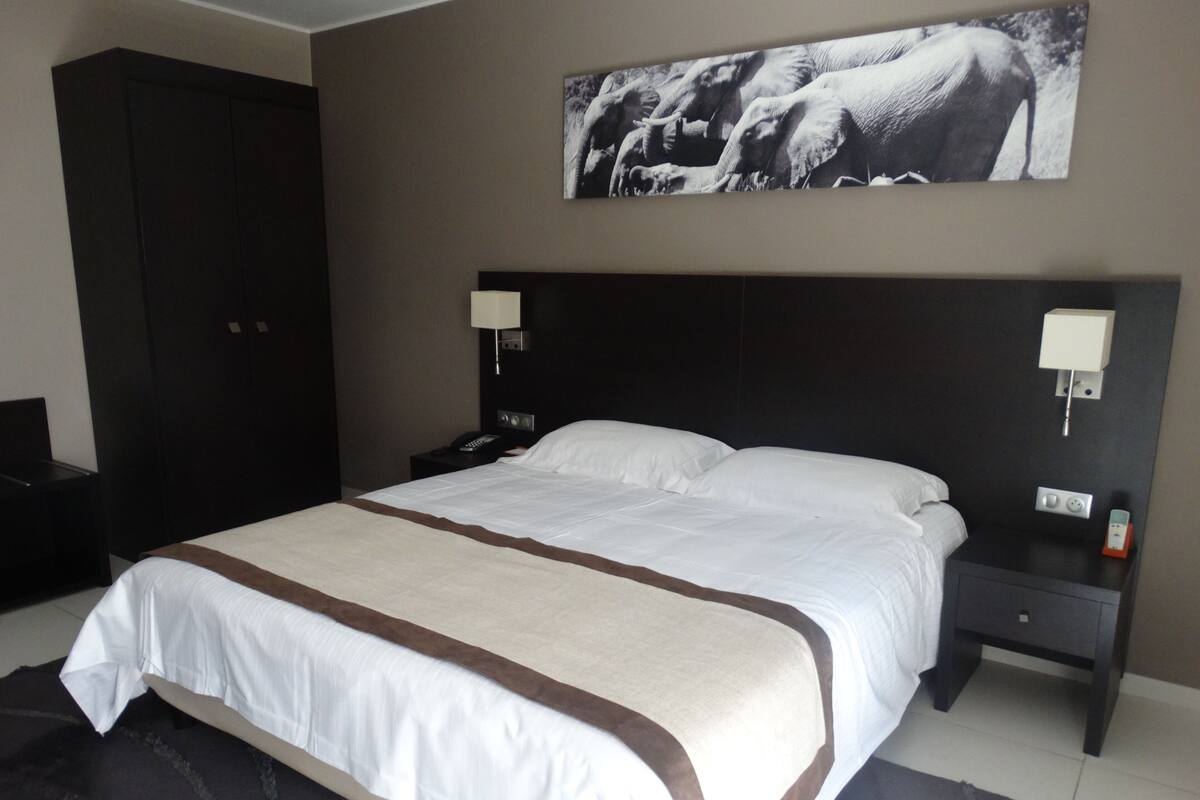 A hotel room with a large bed, two bedside tables, a wardrobe, and a wall-mounted artwork.