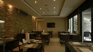 A modern dining area with multiple tables and chairs, a stone wall, and a large window offering a view.