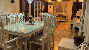Un comedor con mesa de vidrio, sillas blancas, una araña y pared de ladrillo.